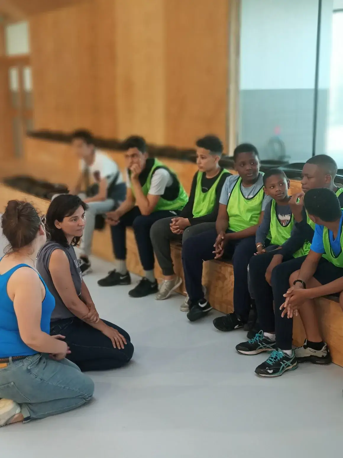Des jeunes en gilets verts assis sur des gradins lors d’une rencontre.