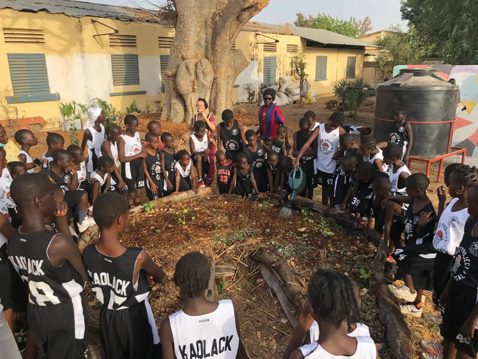 Grand groupe d’élèves rassemblés en cercle dans une cour d’école, sous un arbre