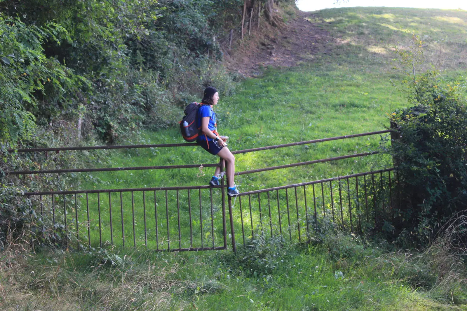 Une jeune femme assise sur une rambarde métallique dans un paysage verdoyant.