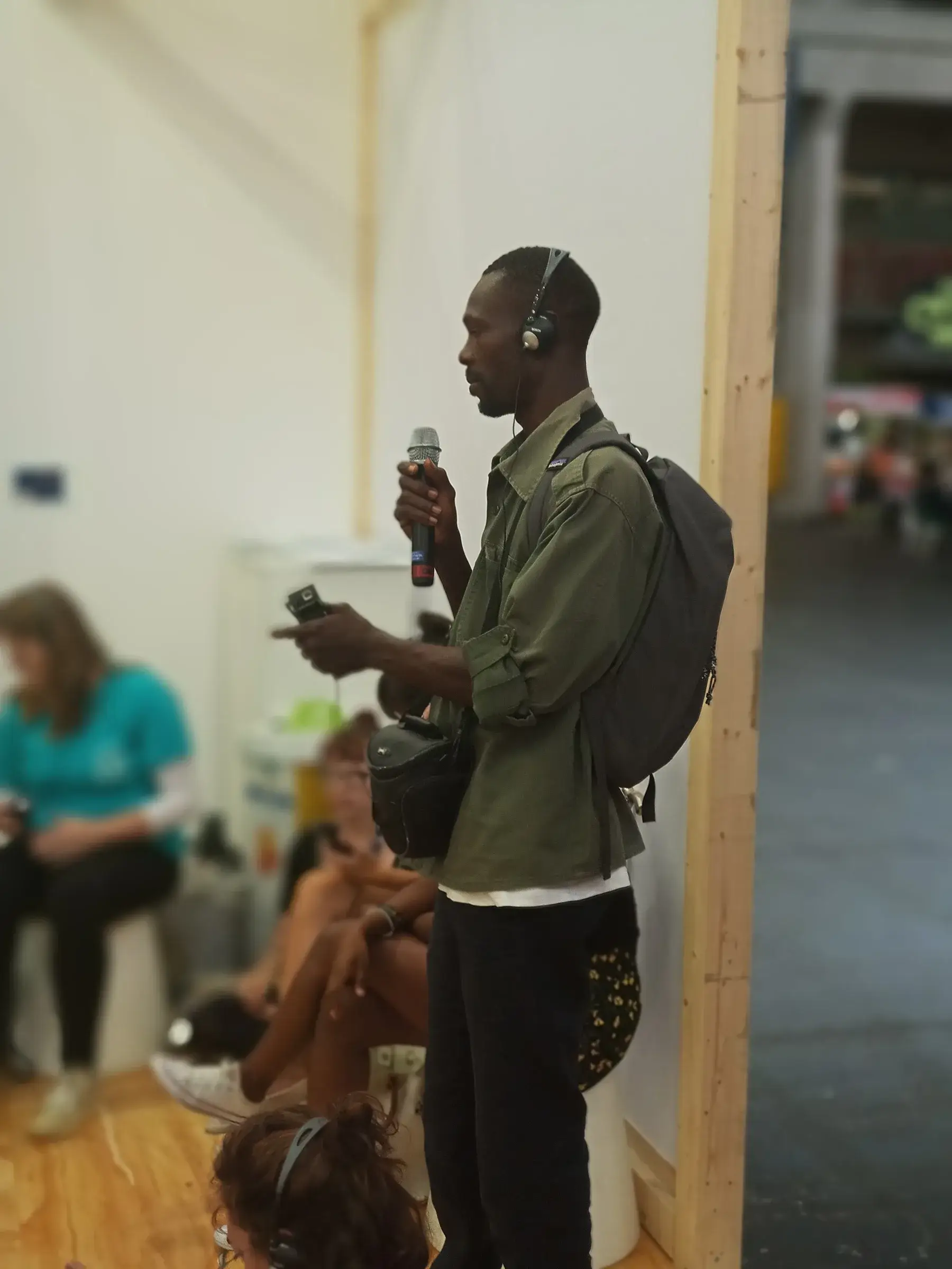 Un homme s’exprime au micro devant un public, dans une salle d’exposition.