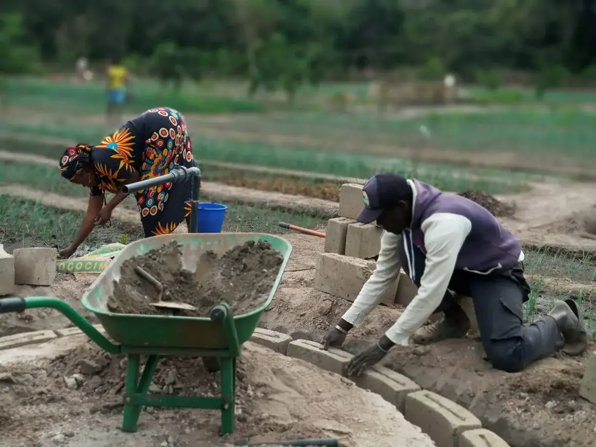 Deux personnes construisent une bordure de jardin en parpaings, brouette de ciment au premier plan