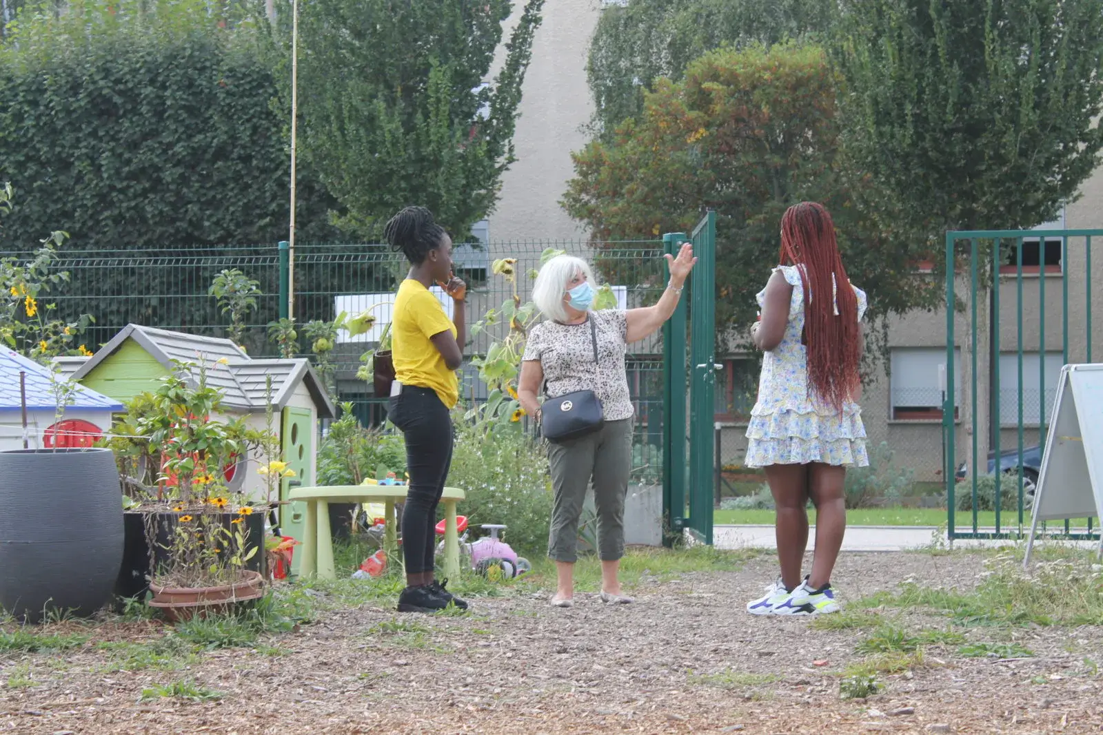 Trois personnes discutant à l’entrée d’un jardin urbain, près d’une serre tunnel
