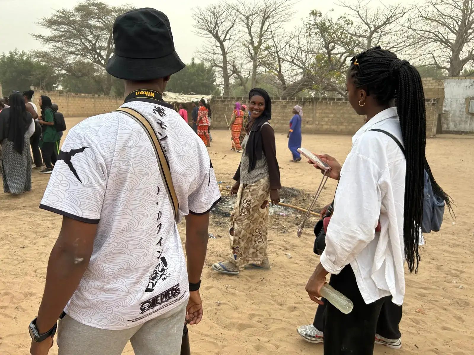 Un homme au chapeau et une femme aux longues tresses marchent de dos sur un chemin de terre, un groupe les précède au loin.