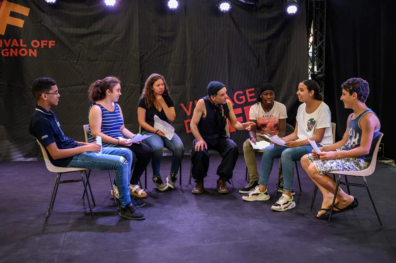 Un groupe de jeunes comédiens répète, assis en cercle sur scène.