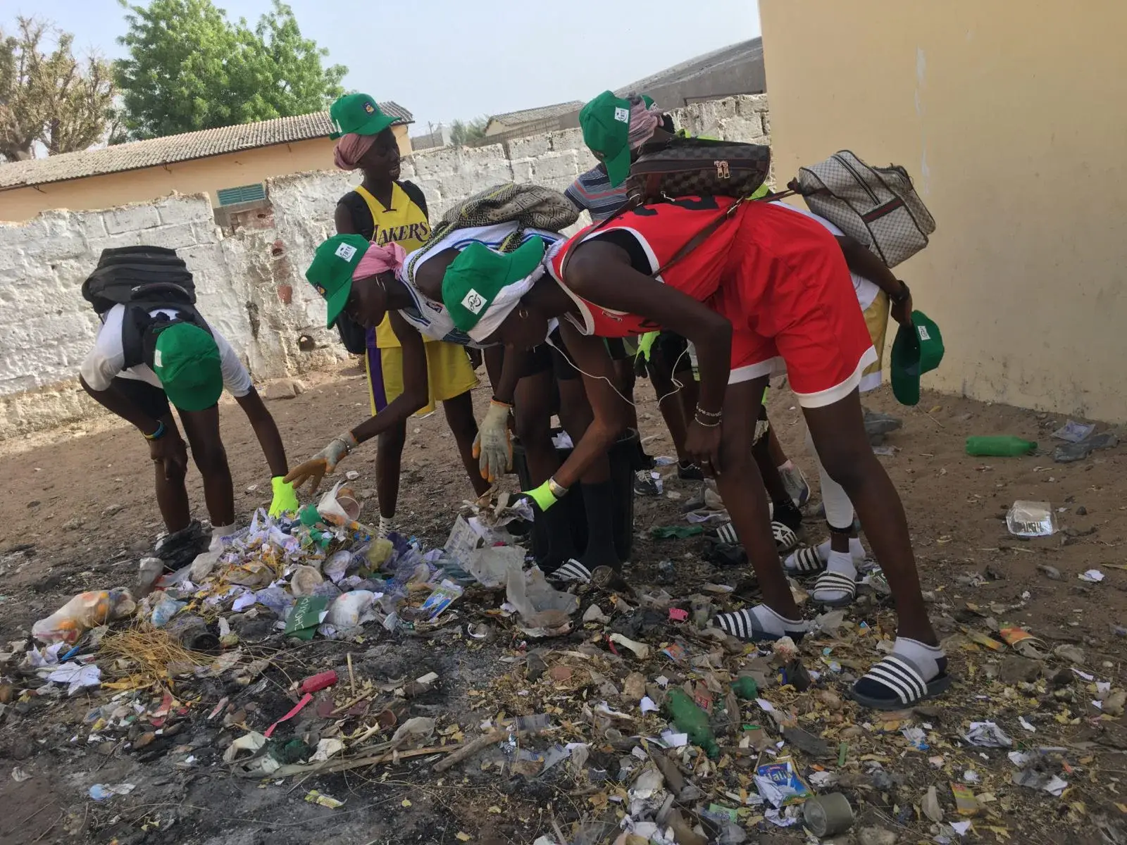 Jeunes en tenue verte ramassant des bouteilles et des déchets plastiques dans la cour