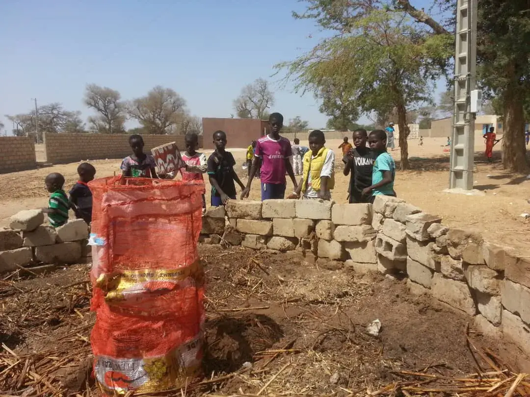 Des enfants posent derrière un jardin en trou de serrure et sa colonne de compost entourée d’un filet orange