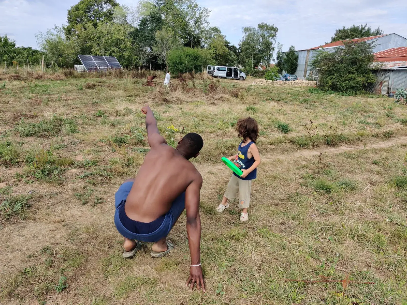 Un membre de l’écolieu montre le ciel à un enfant tenant un arrosoir.