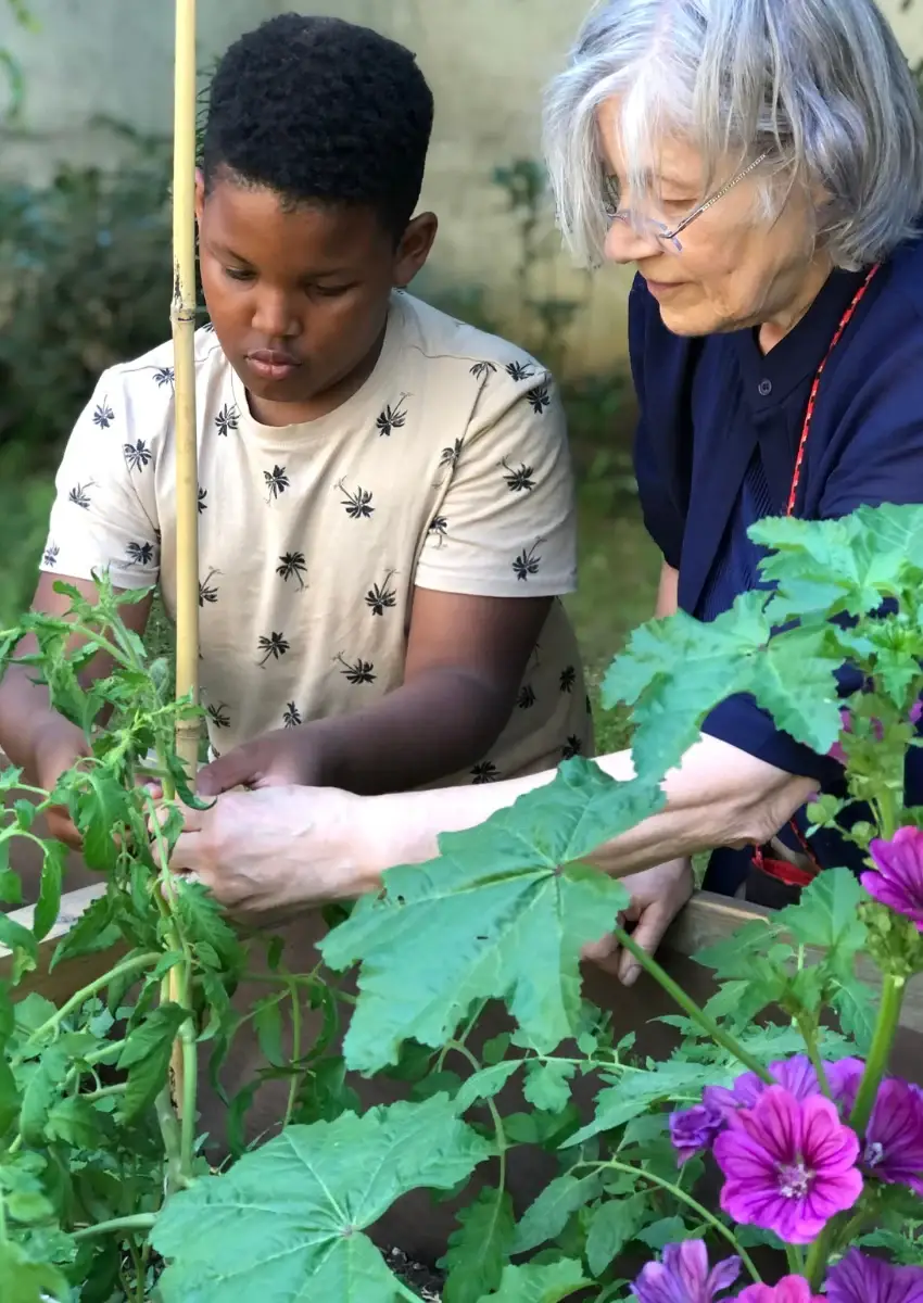 Une femme âgée et un jeune homme examinent ensemble les feuilles d’une plante dans un jardin.