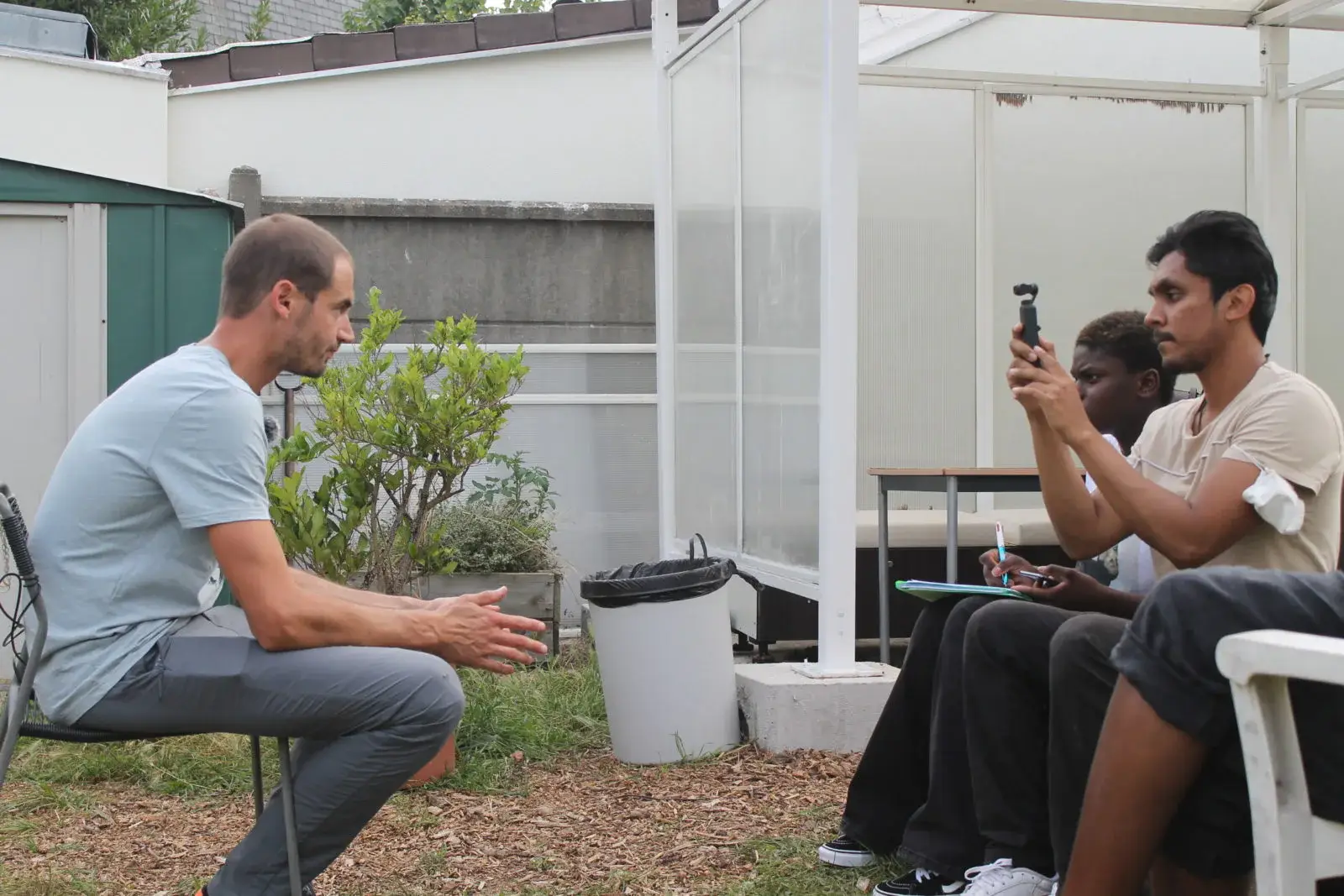 Un homme assis dans un jardin, interviewé par une personne qui enregistre avec un téléphone