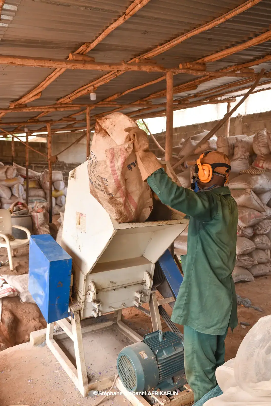 Un ouvrier en tenue de protection alimente une machine de broyage avec un sac