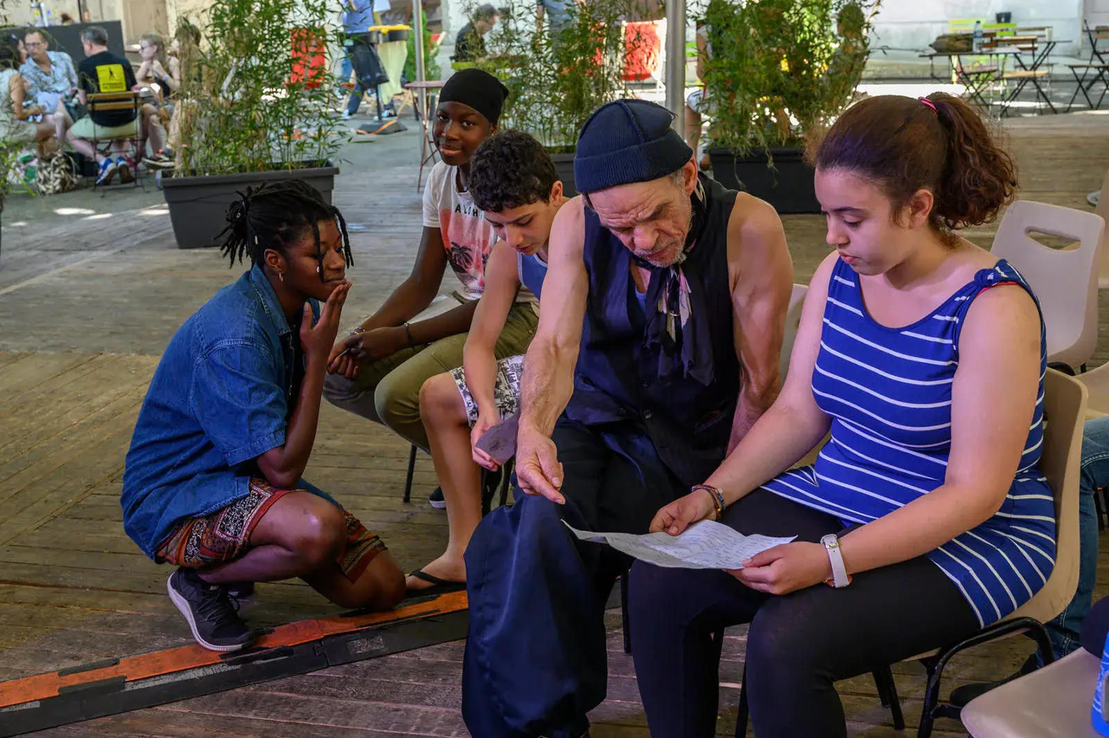 Des jeunes et un comédien répètent autour d’un texte, dans un espace végétalisé.