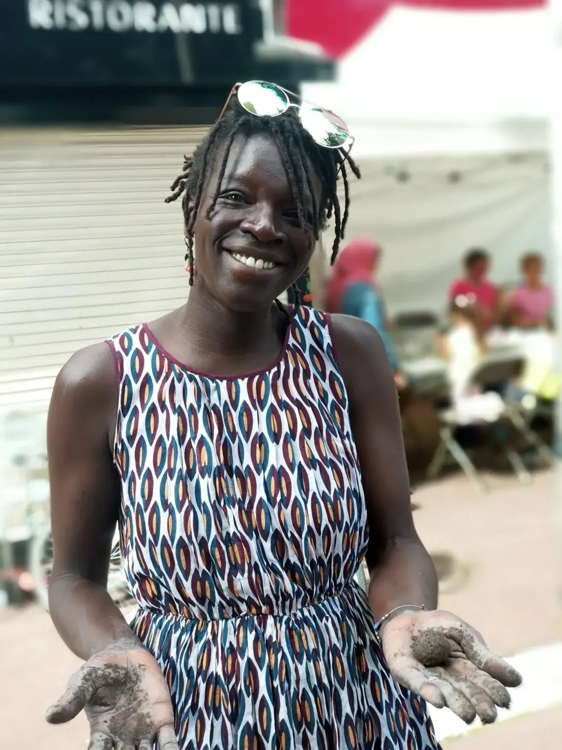 Une femme souriante en haut coloré, avec des enfants en arrière-plan.