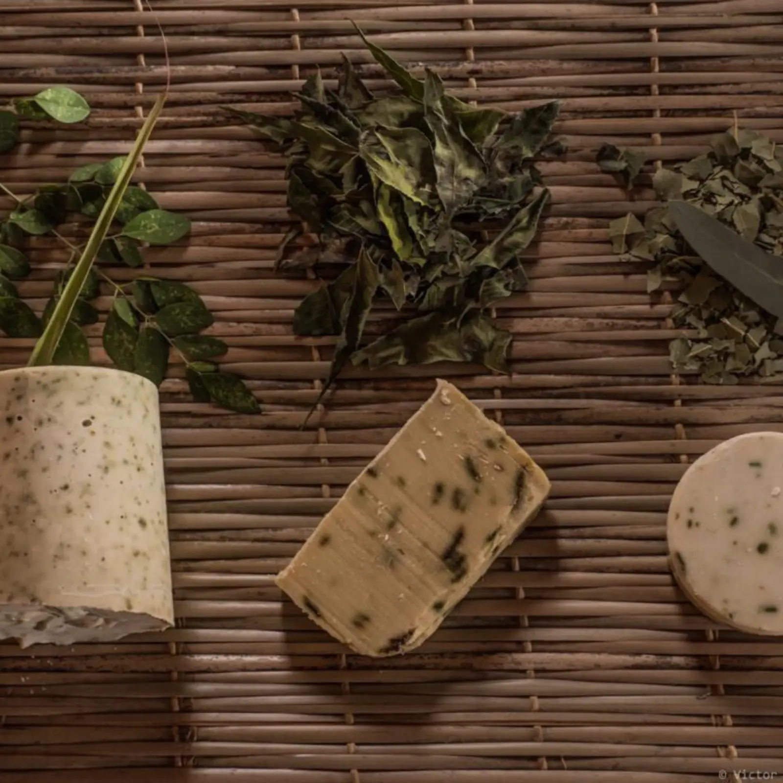 Des savons naturels, des plantes aromatiques et un mortier sur une natte.