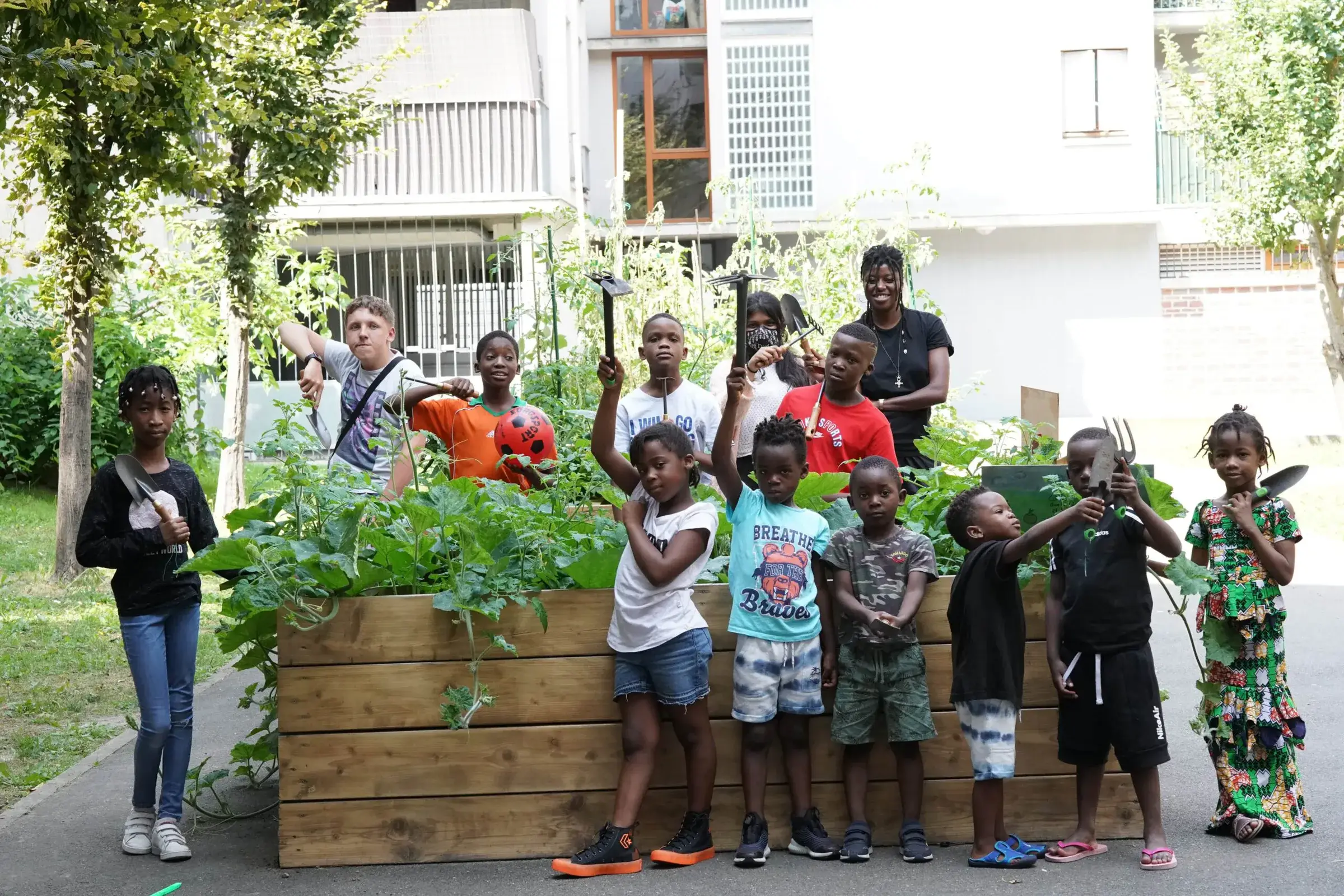 Petits et grands posent derrière un grand bac de culture en bois rempli de plantes.