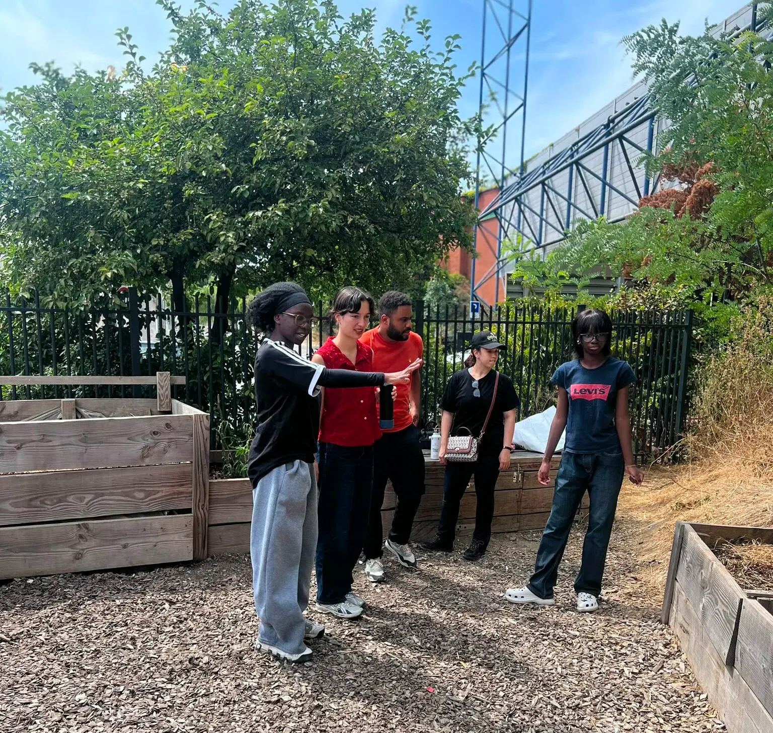 Un groupe échange dans un jardin potager, devant des bacs en bois et des immeubles.
