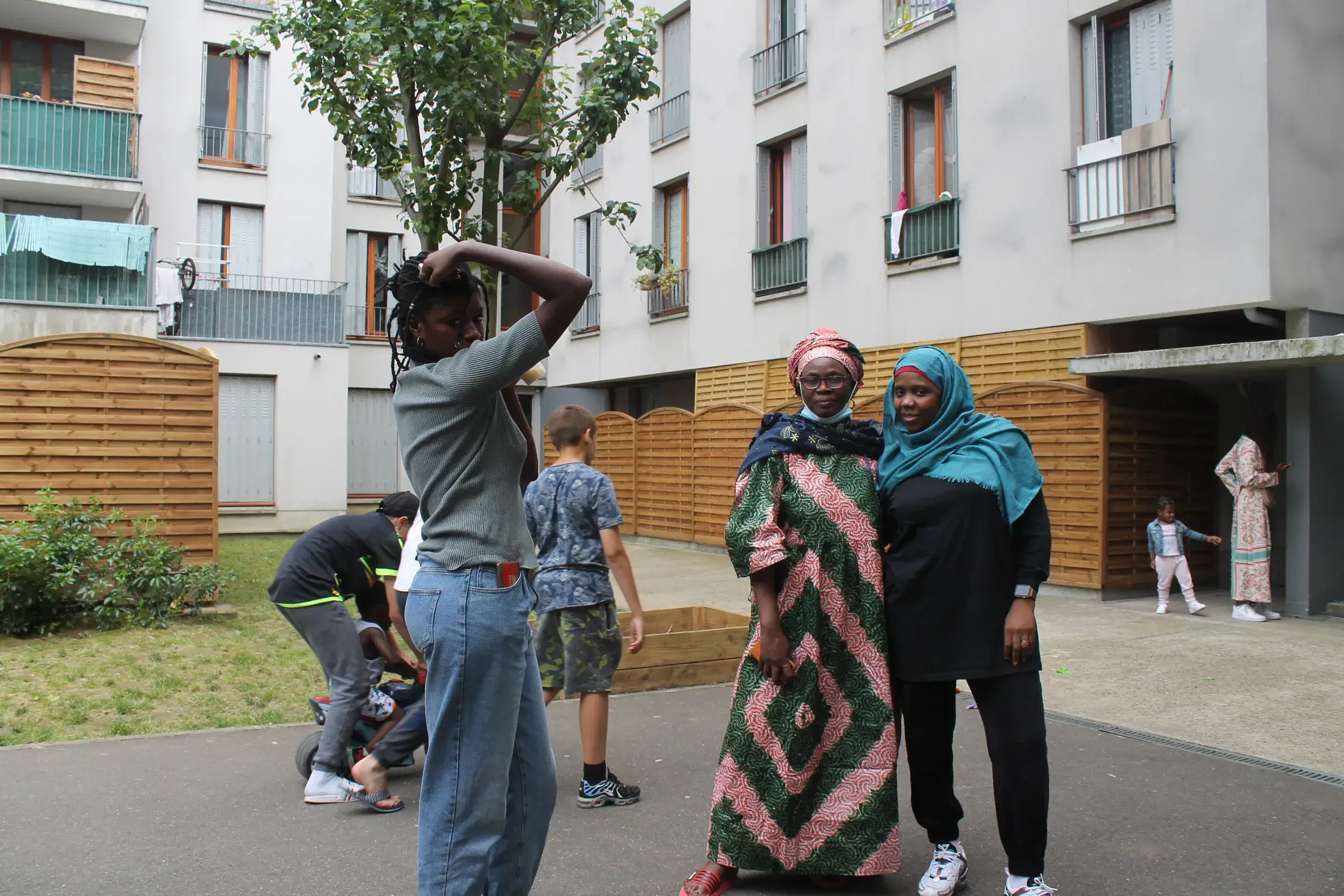 Un homme en sweat bleu s’adresse au groupe devant un bac de culture, dans une cour d’immeuble.
