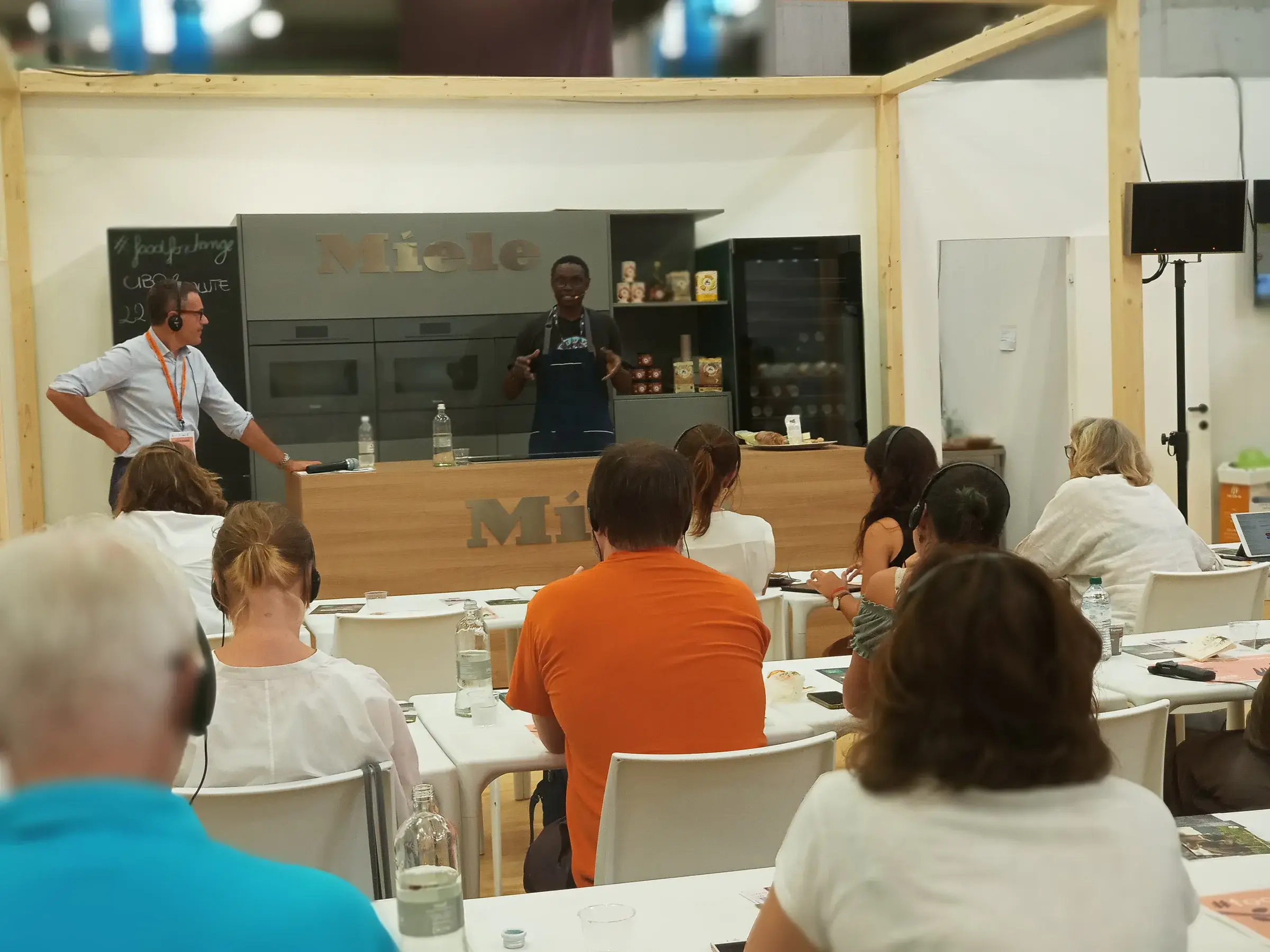 Des spectateurs attablés suivent une démonstration de cuisine.