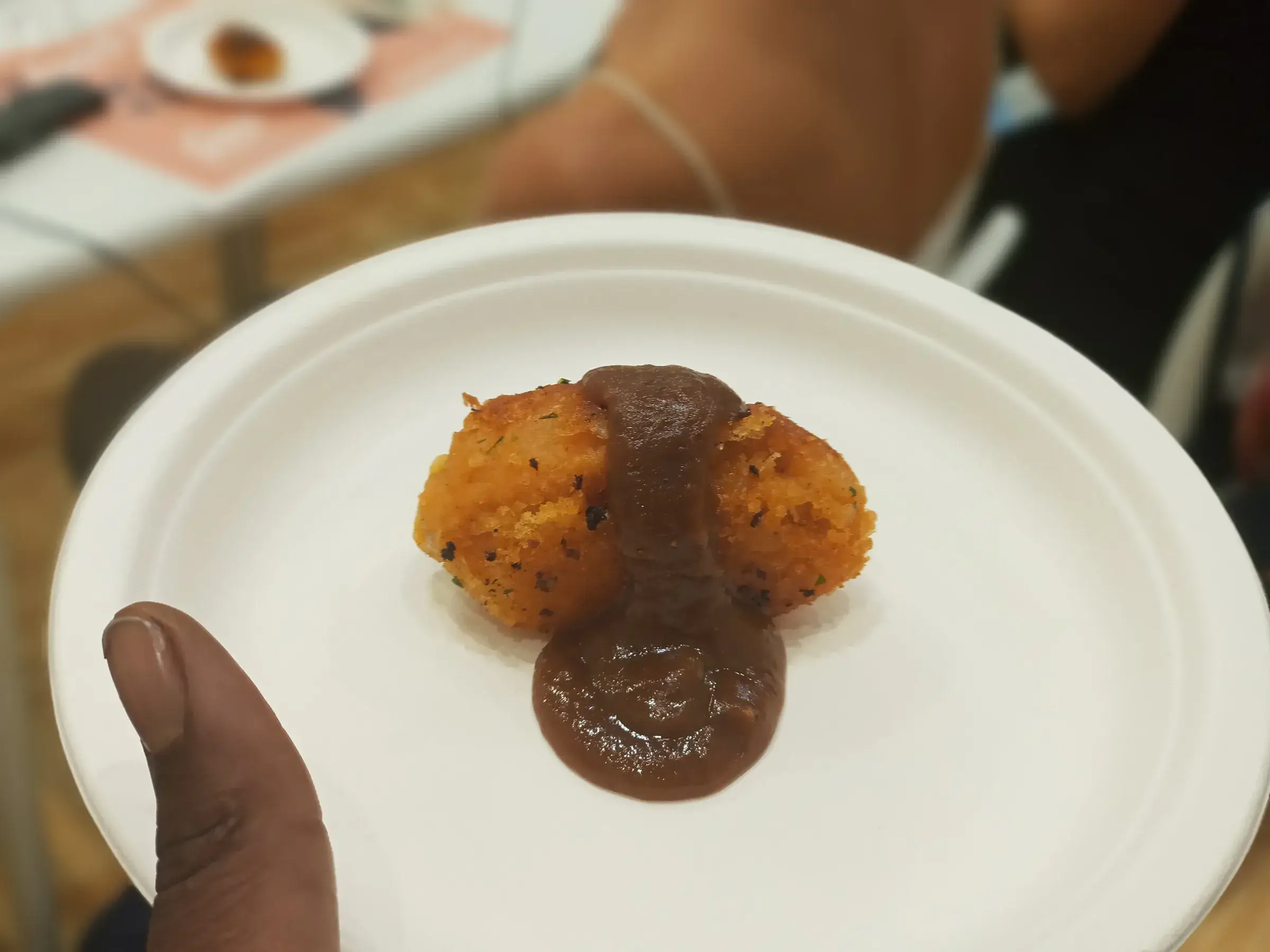 Une main tient une assiette avec des beignets et une sauce sombre.