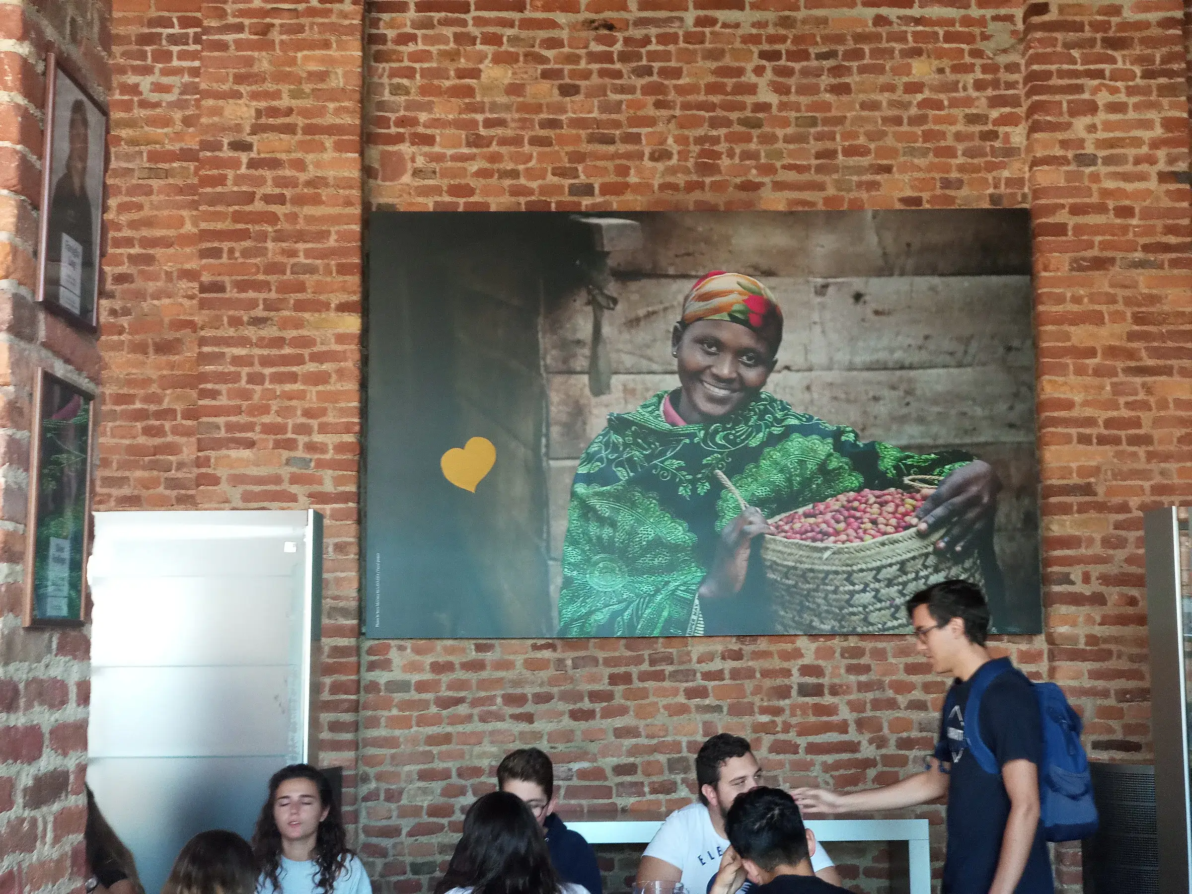 Une grande photo d’agricultrice exposée sur une façade en briques, au-dessus de visiteurs.