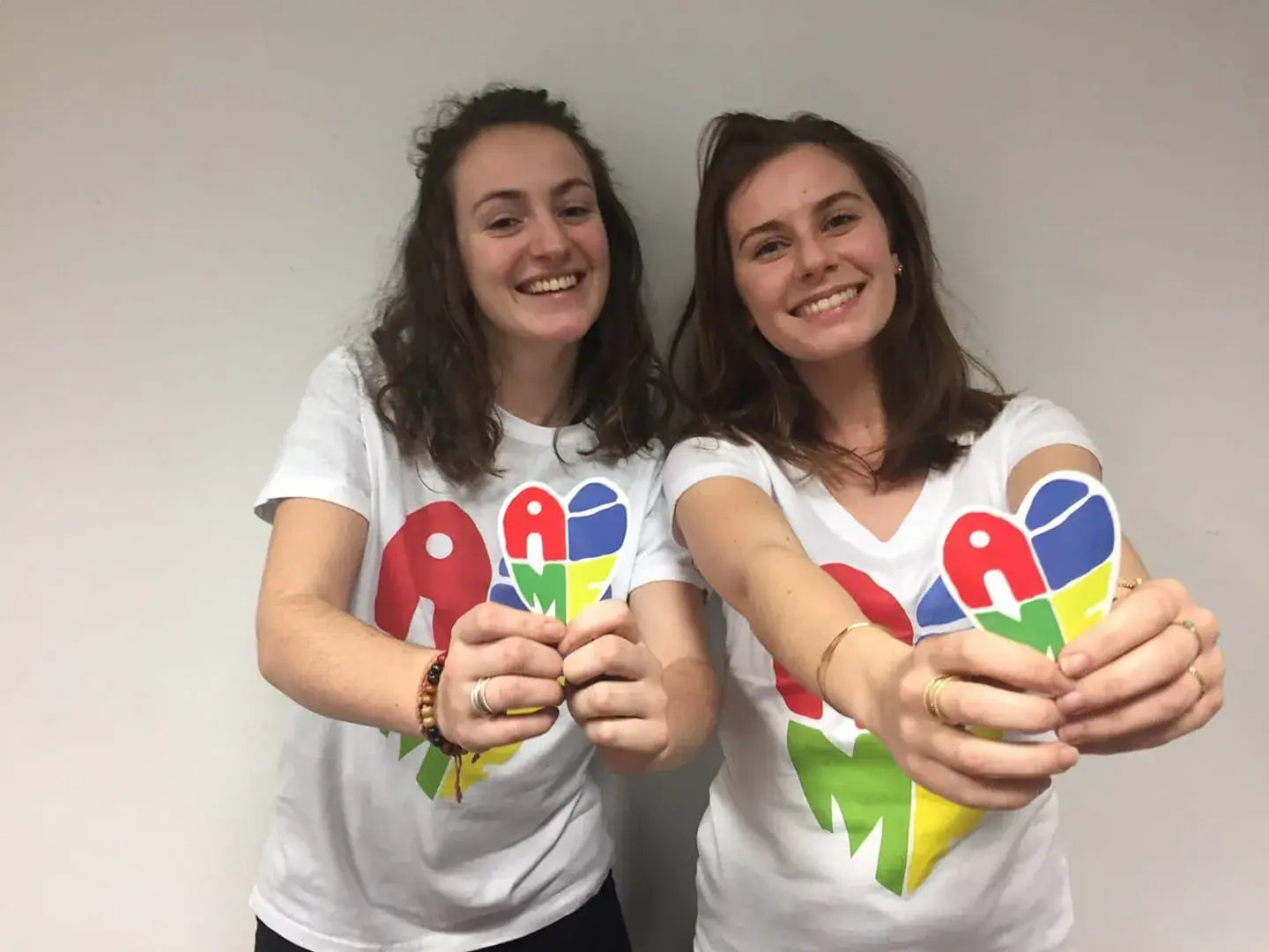 Deux bénévoles d’A.I.M.E en t-shirts blancs forment un cœur avec leurs mains.