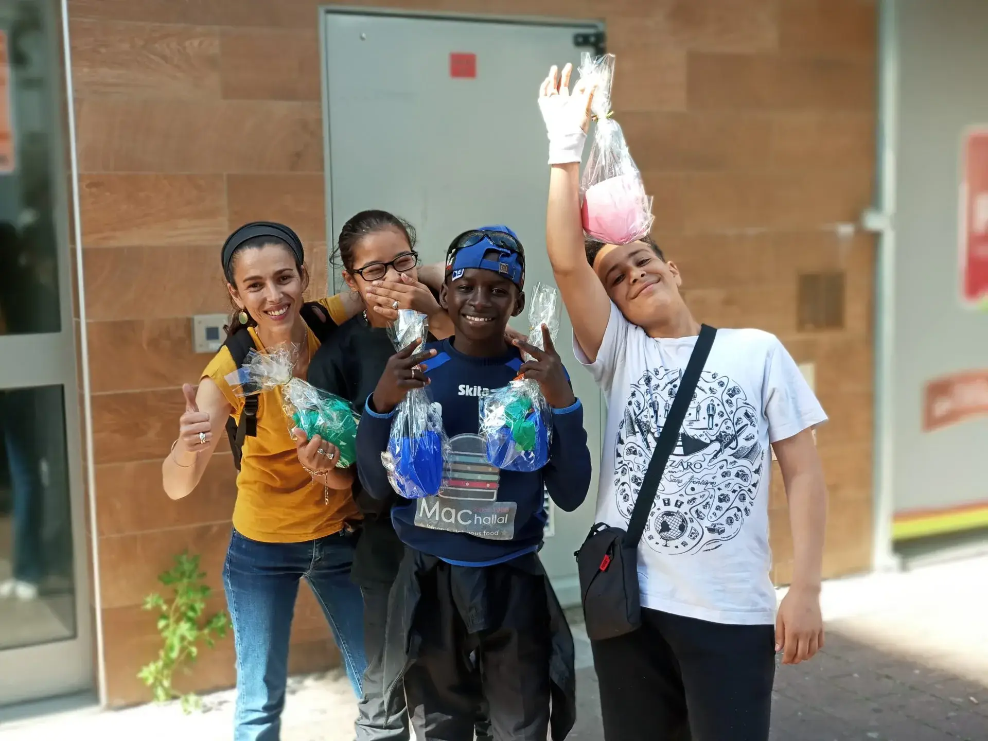 Quatre jeunes brandissant des sacs de déchets collectés devant un bâtiment.
