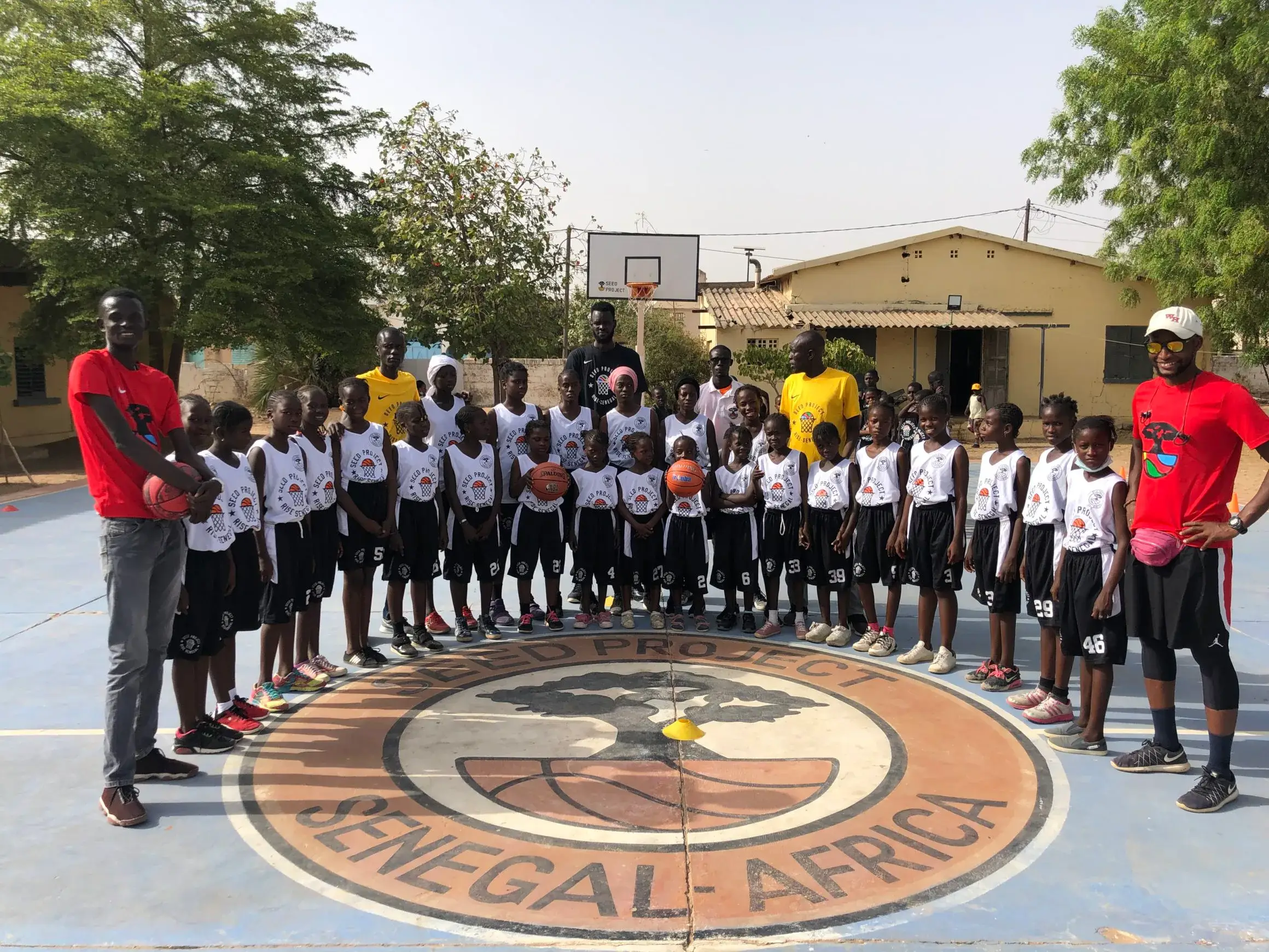 Équipes de jeunes basketteurs alignées sur un terrain extérieur, encadrées par deux coachs