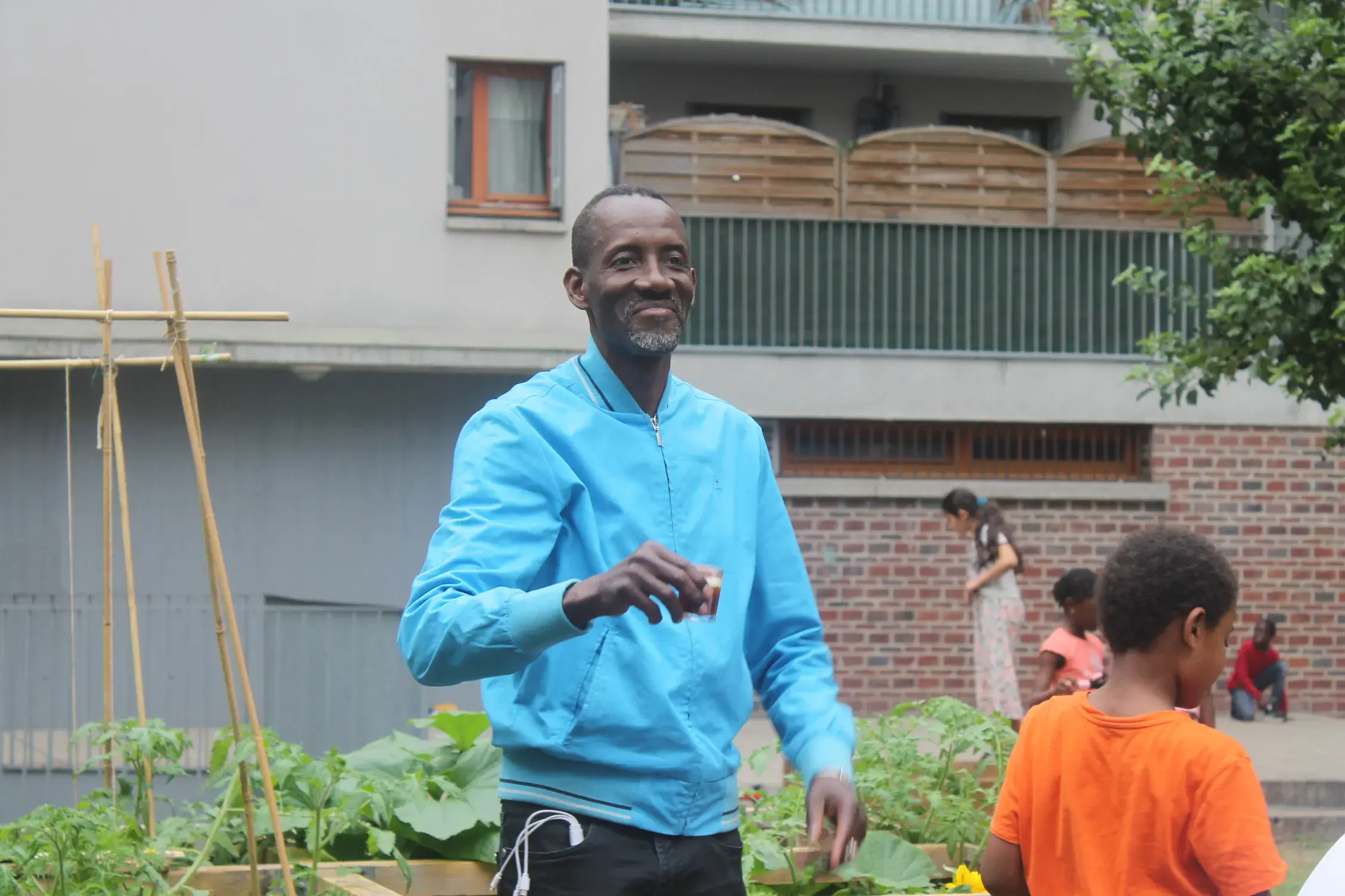 Un homme souriant en sweat bleu, debout dans un jardin potager.