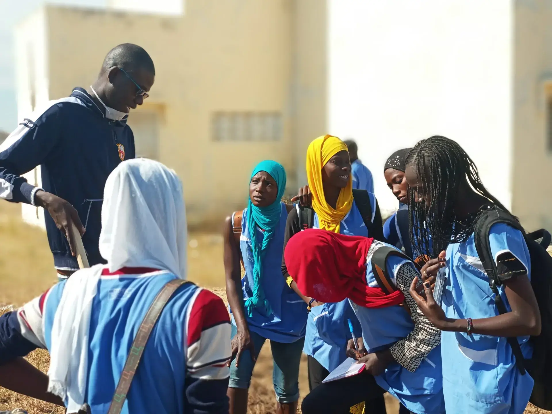 Des élèves en uniforme bleu réunis autour d’un adulte dans la cour d’une école.