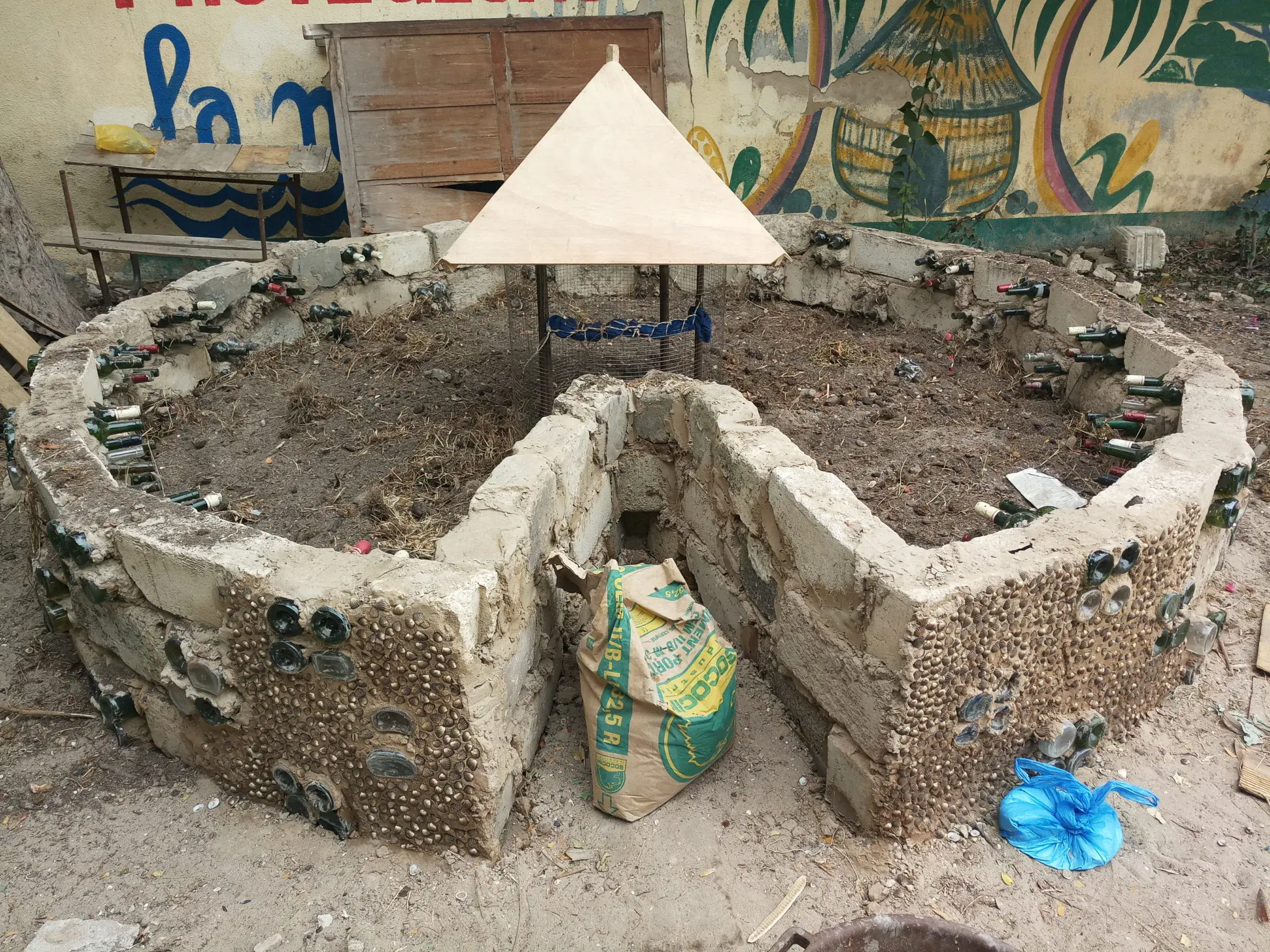 Jardin en trou de serrure construit en pierres et bouteilles recyclées autour d’une colonne de compost